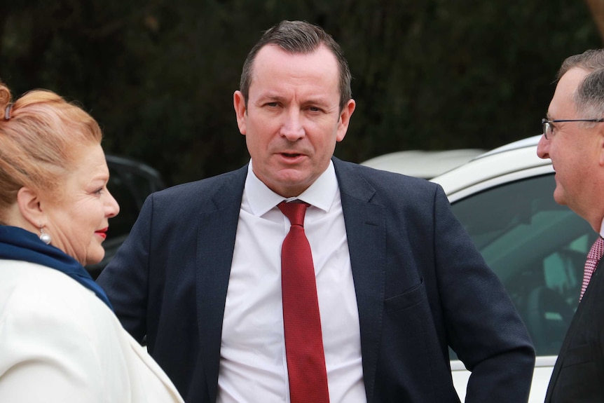 A mid-shot of WA Premier Mark McGowan standing outside State Parliament in a conversation with two people.