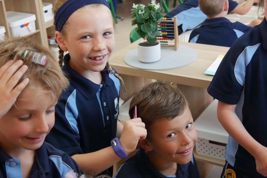 A group of Year 1 and pre-primary students pose for a photo in class as one girl combs a boy's hair.