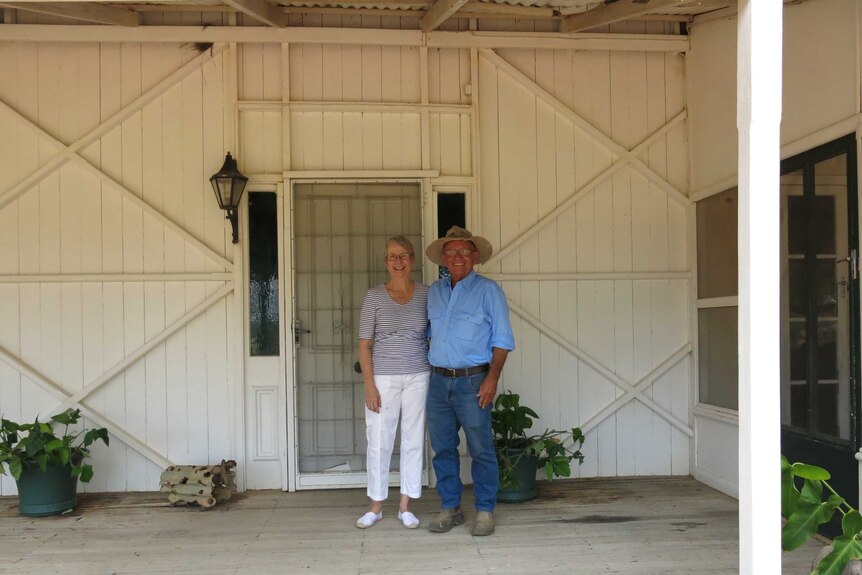 The station owners standing together outside their front door of the wooden home.