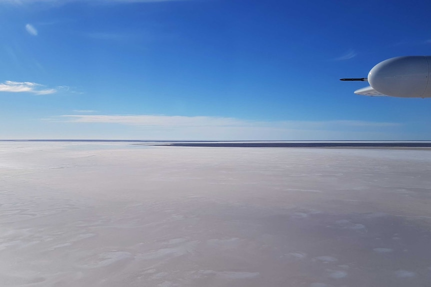 An aerial shot of a dry expanse of Lake Eyre below a blue sky and a plane wing.