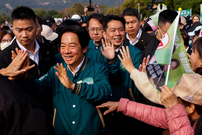 A man surrounded by a crowd smiles and waves.