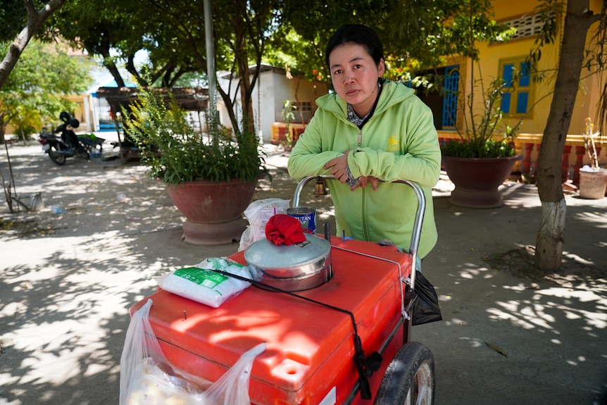 A woman wearing a lime green zipped hoodie leans against a cart with a large esky and ice on top