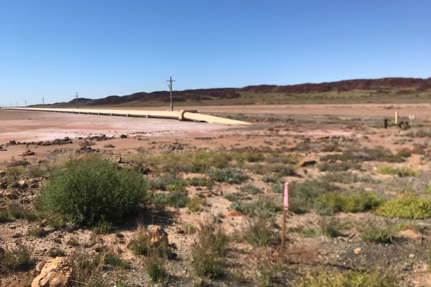 A dusty patch of land with a water pipe in the background