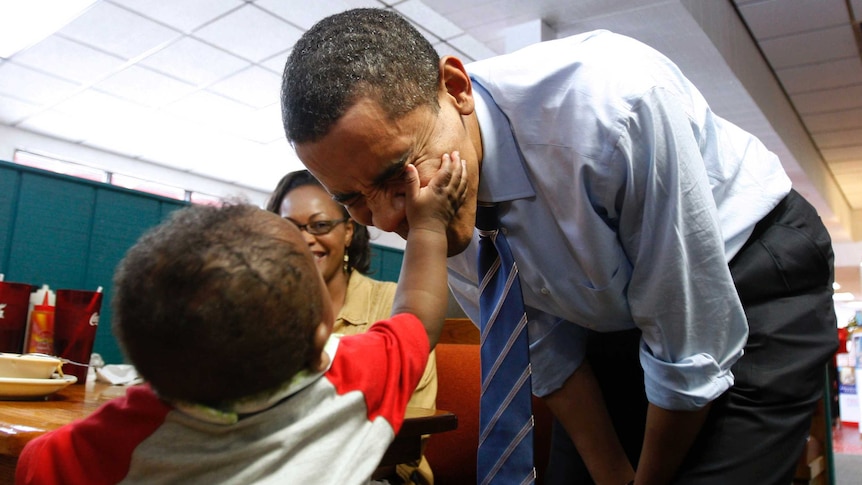 Barack Obama has his cheek touched by a 7-month-old.