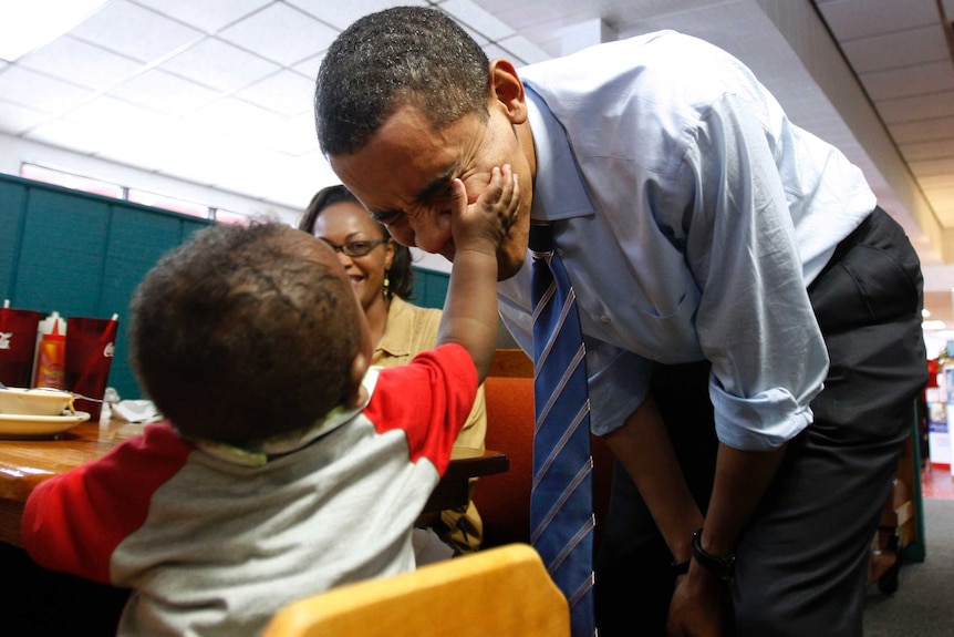 Barack Obama has his cheek touched by a 7-month-old.