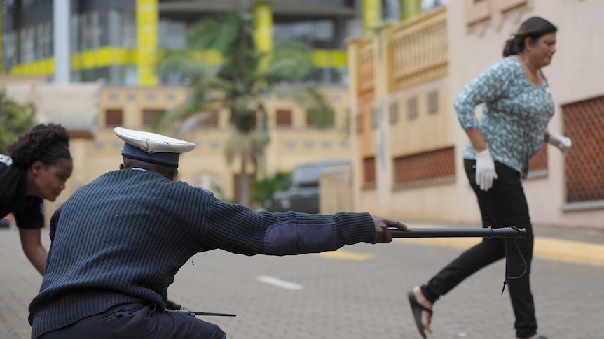 Kenyan police officer guides bystanders to cover as gunshots heard from mall