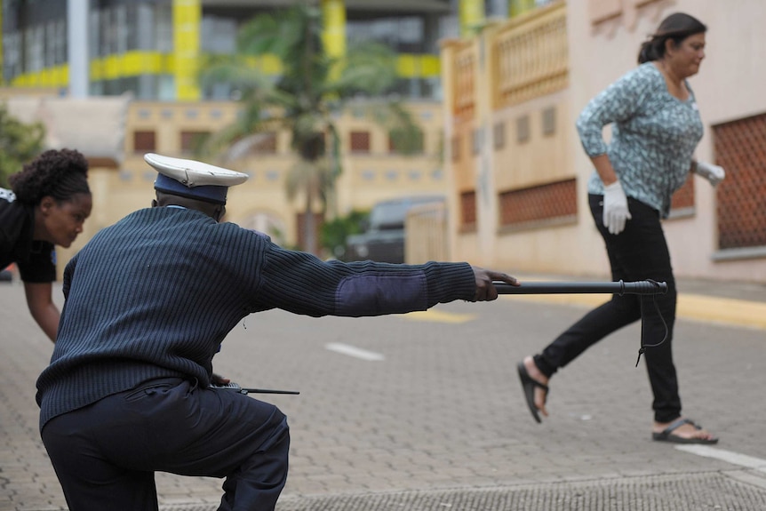 Kenyan police officer guides bystanders to cover as gunshots heard from mall