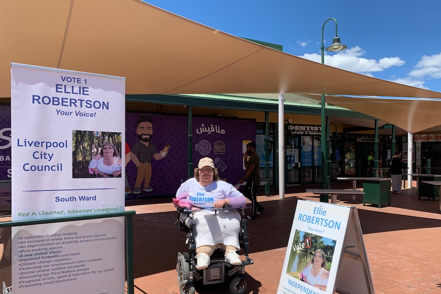 Ellie Robertson in her wheelchair in between two signs saying vote for her in the liverpool city council