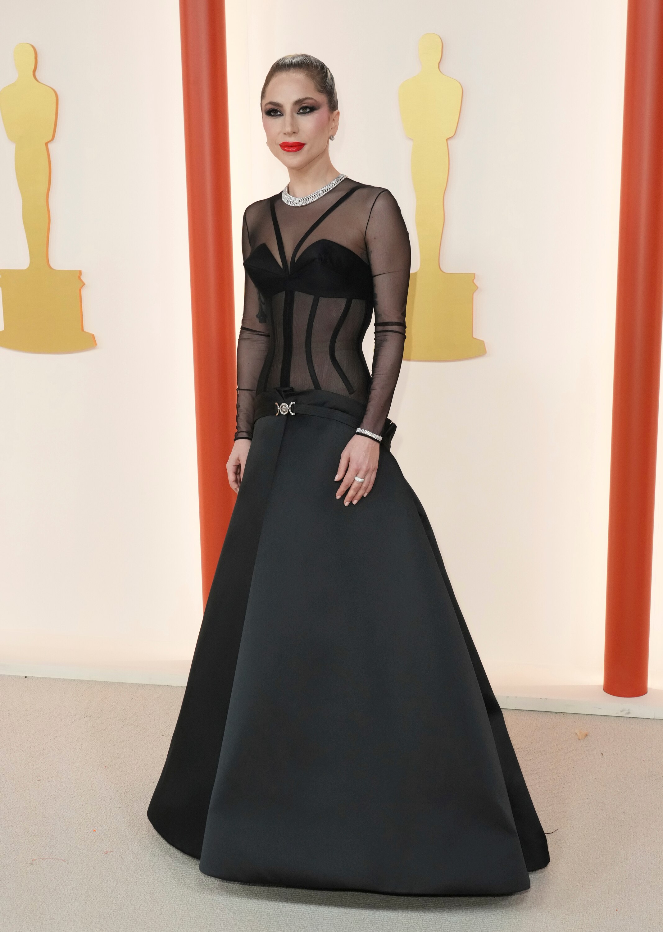 Lady Gaga wearing a floor-length black gown with a silky fully skirt and a sheer top with long sleeves and visible boning