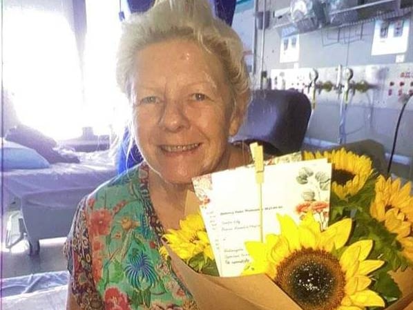 Woman smiling with flowers on a hospital bed. 