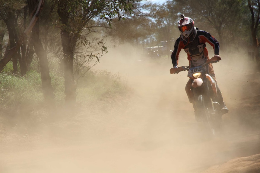 A dirtbike tears through the bush, leaving a trail of dust behind it