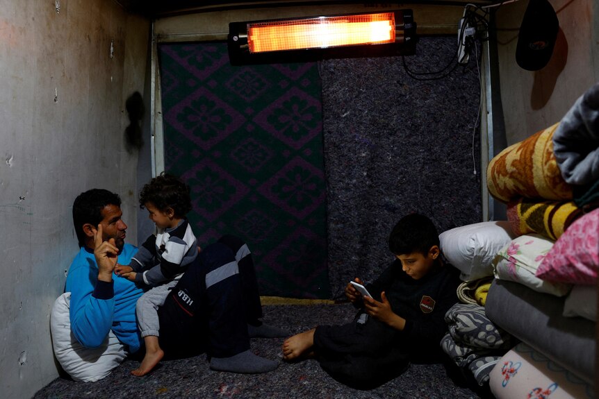 A father and two boys sit on the floor in a small room.