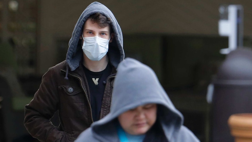 A man wearing a hoodie walks outside wearing a face mask amid the coronavirus outbreak in the United States