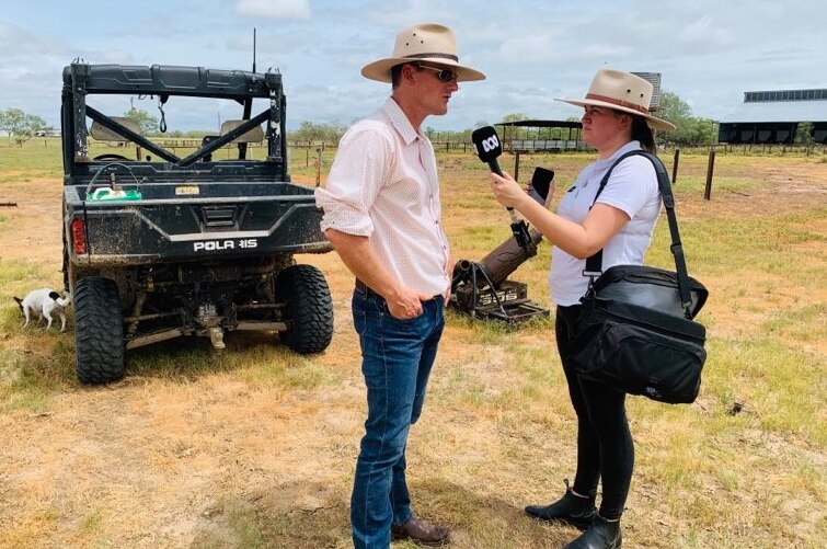 A woman with a radio microphone interviewing a man in a farm setting.