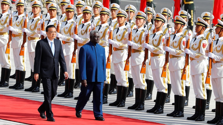 一名中国官员和所罗门群岛官员走过红地毯，旁边是列队的中国军队。