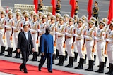 A Chinese official and Solomon Islands official walk down a red carpet, next to lines of Chinese troops in formation.