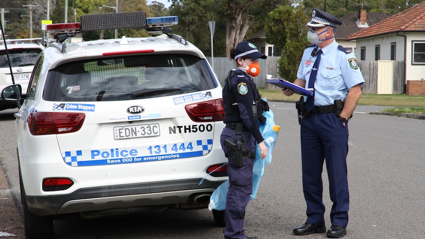 Police wearing face masks stand next to a police car outside a block of units