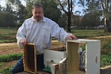 An unhappy looking man holding his beekeeping equipment, without any bees