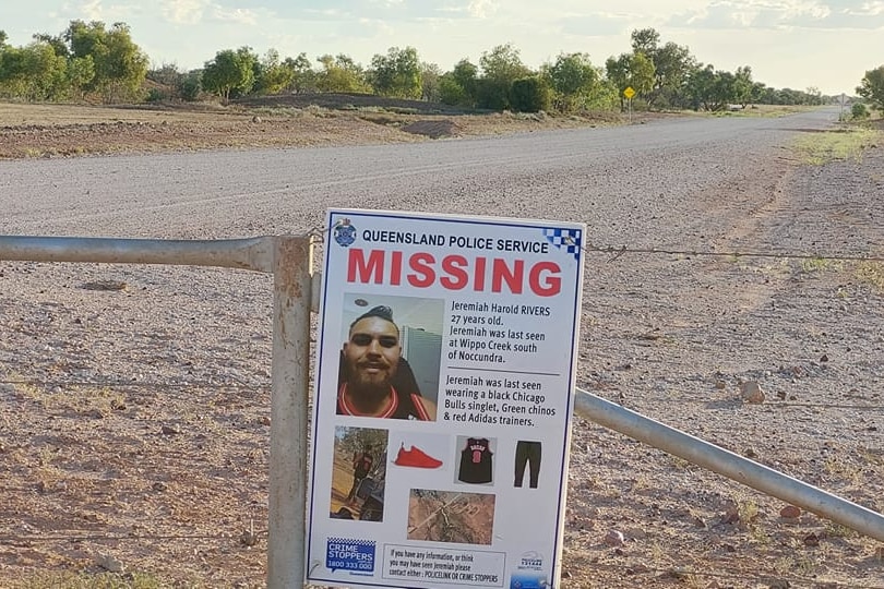 A missing person poster on a barb wire fence next to a dirt road.