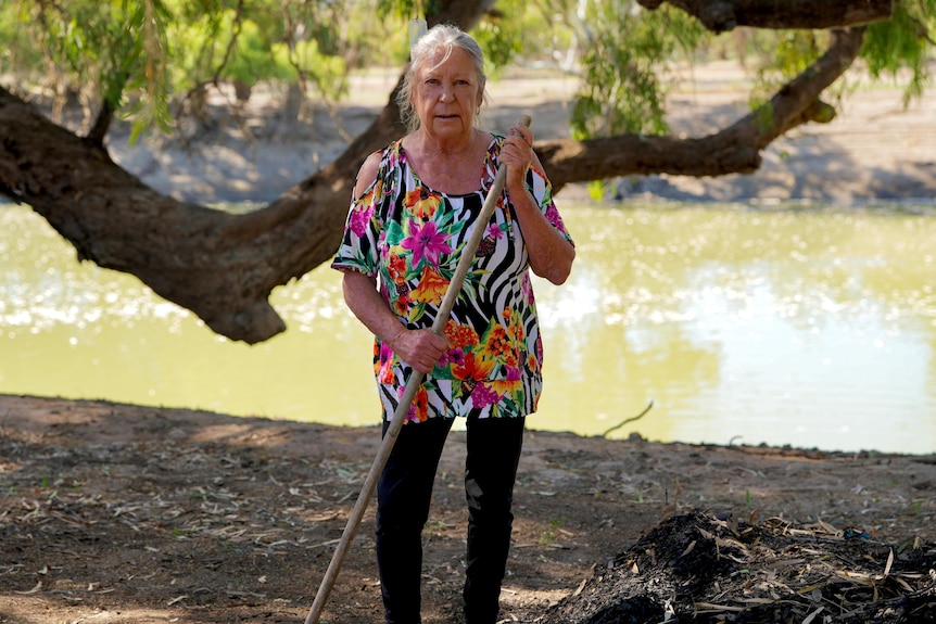 Woman standing in front of a river holding a rake