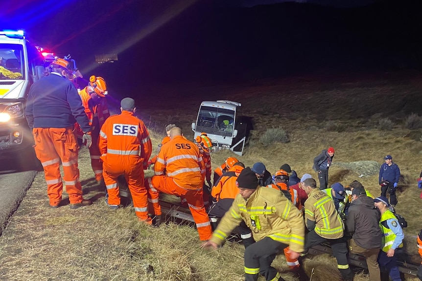 rescue crews help children up an embankment with a crashed bus sitting in the bakground. 