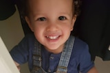 A little boy in overalls smiles