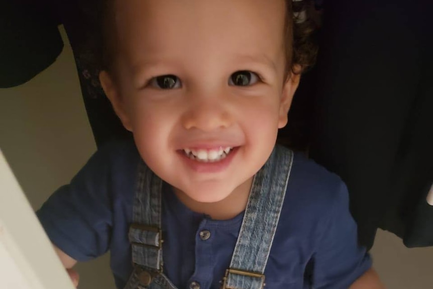 A little boy in overalls smiles