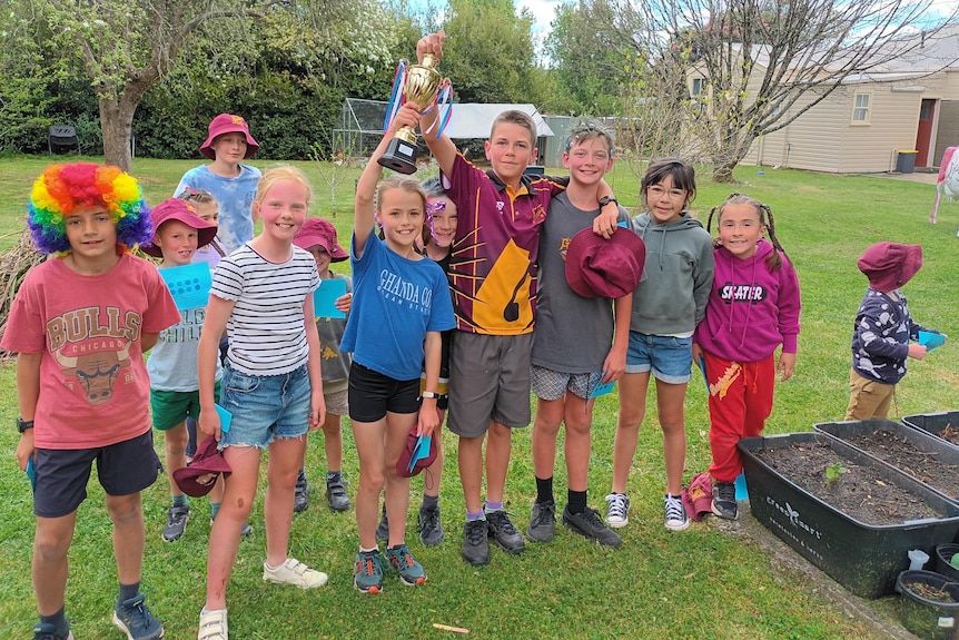 primary school students gather together, two in the middle hold up gold trophy