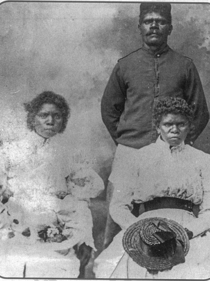 Black-and-white-white photo of Indigenous man Jack Noble, with two Aboriginal women sitting in front of him.