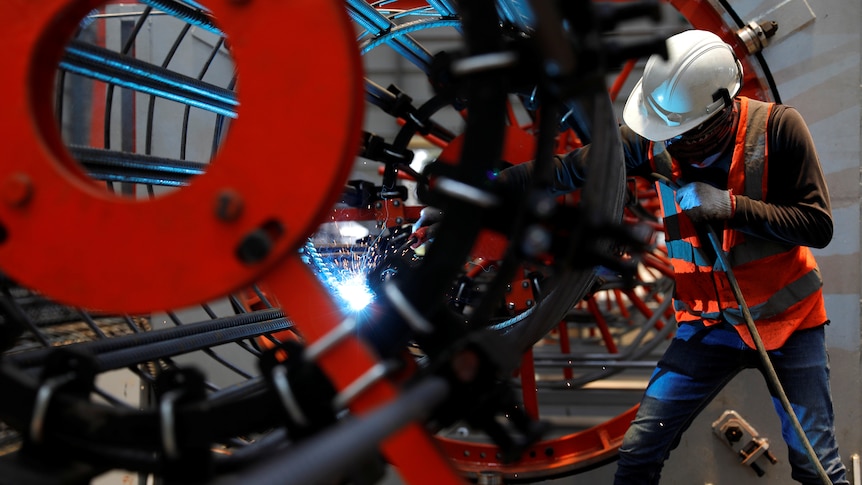 A worker welds as he installs bore-pile devices at a steel fabrication of rebar cages .