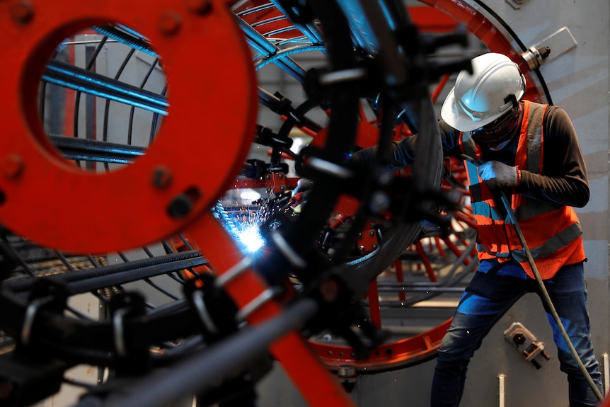 A worker welds as he installs bore-pile devices at a steel fabrication of rebar cages .