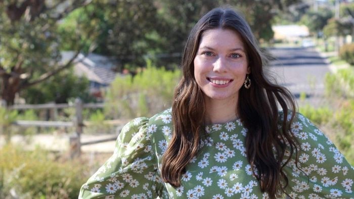 A woman with long brown hair and a green blouse smiles while looking at the camera.