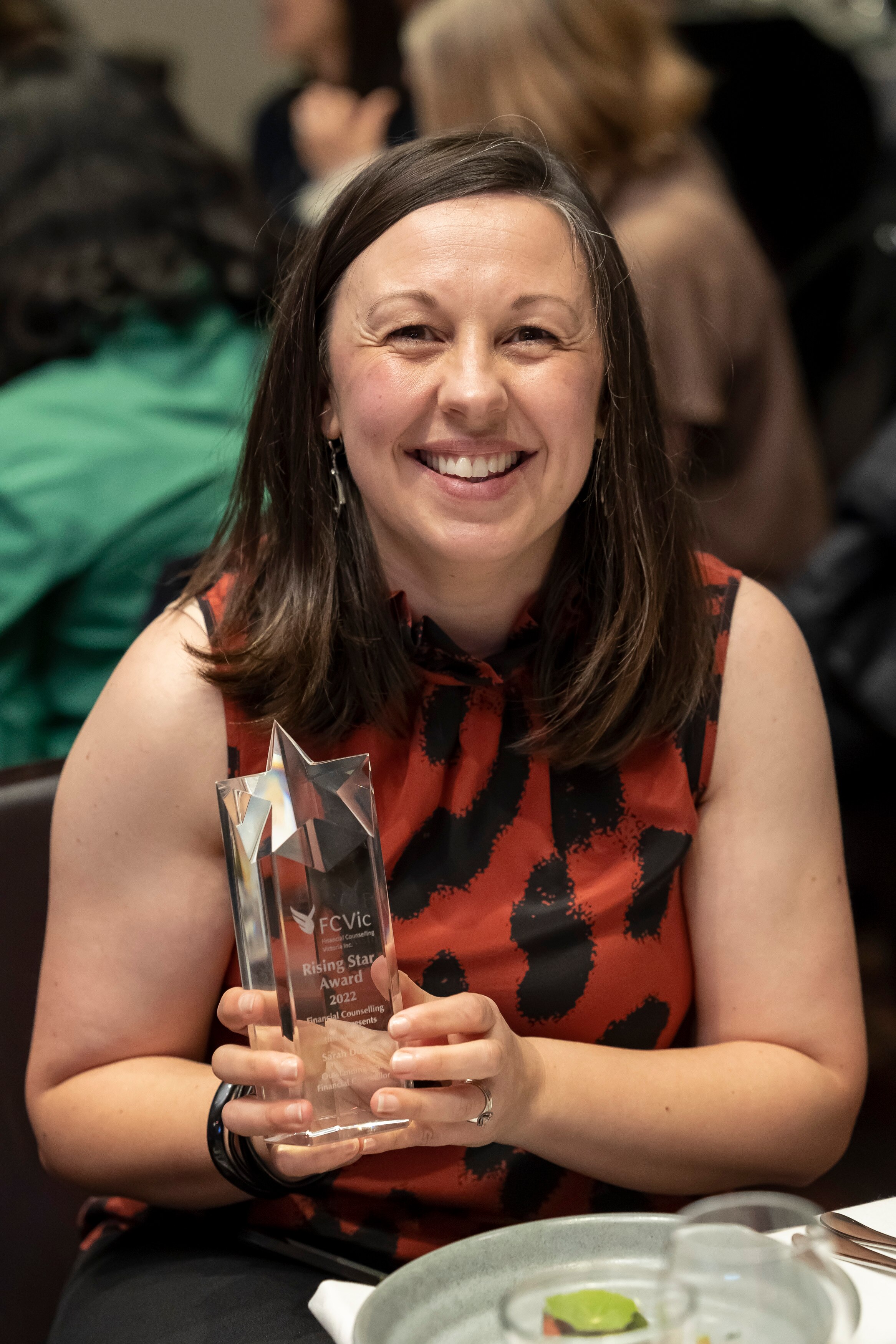 Sarah Duane sonríe, sosteniendo un trofeo del premio de vidrio