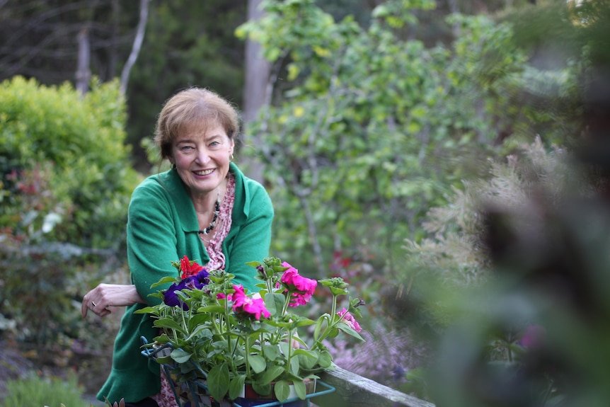 A woman smiling at the camera while standing in front of colourful flowers.