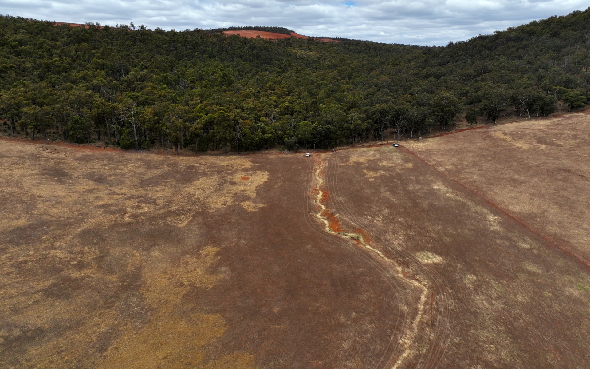 Tierra roja y una línea clara donde comienza el matorral y la vegetación, una mina al fondo.