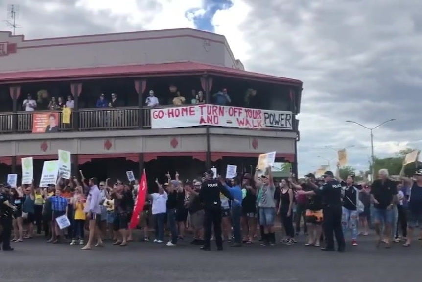 A large group of people stand on the corner outside a pub, hold signs in support of coal mining.