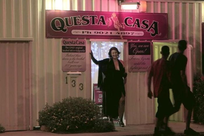 A scantily-dressed woman standing outside of historic brothel while two men walk past.