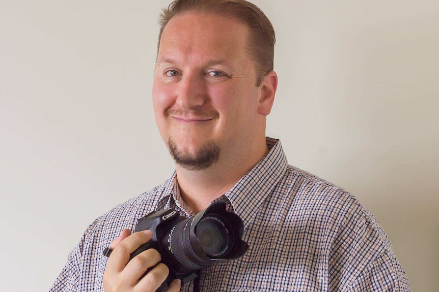 Nick Verburgt holds a camera and smiles for a photo