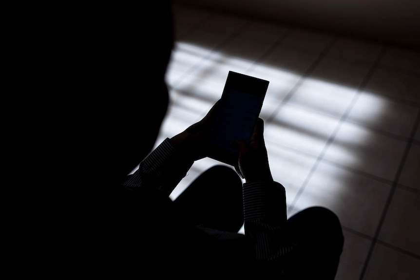 Woman in silhouette sitting and tapping on a mobile phone.