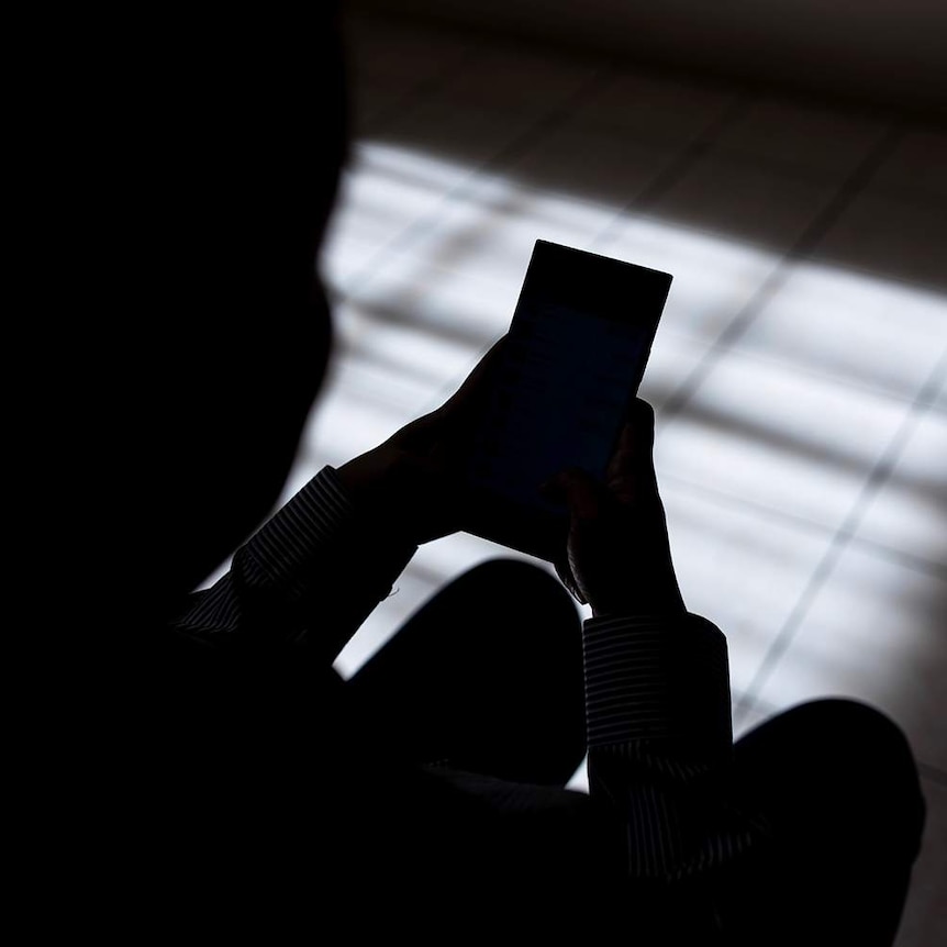 Woman in silhouette sitting and tapping on a mobile phone.