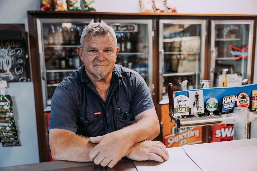 A publican standing behind the bar of his pub next to beer taps.