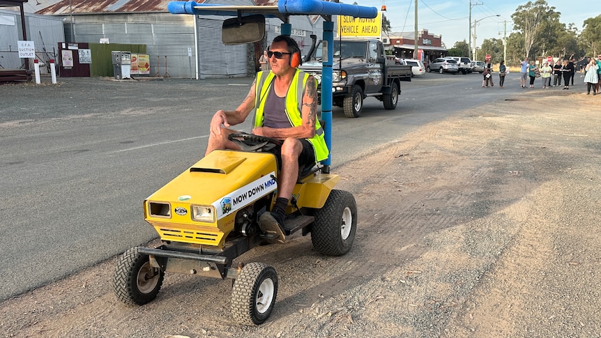 man in fluro vest sits on top of bright yellow ride on mower