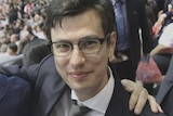 A man in a suit smiling in a crowd.