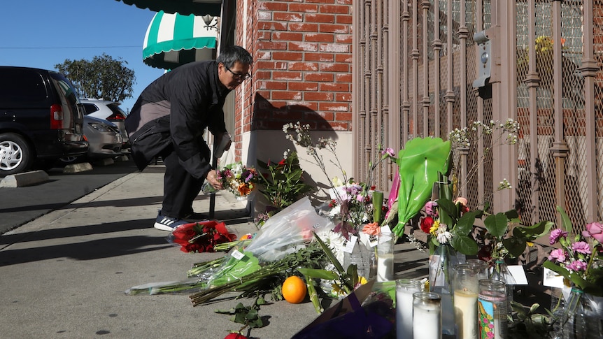 A man places flowers at a vigil. 