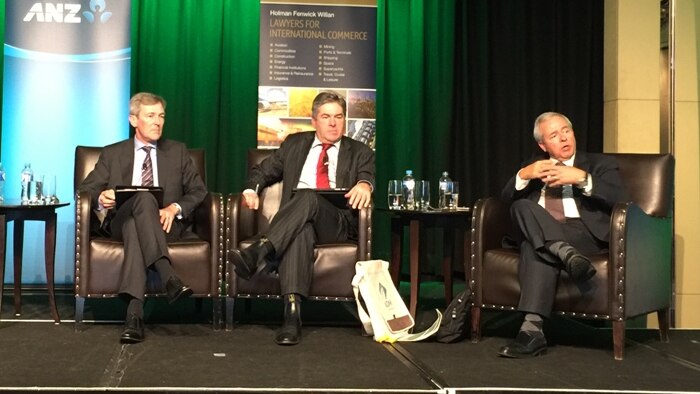 Three men in suits sit on stage in separate chairs