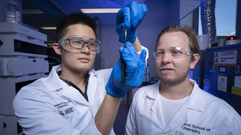 Scientists Zhen Jiang and Luke Connal in lab coats stretch a piece of hydogel