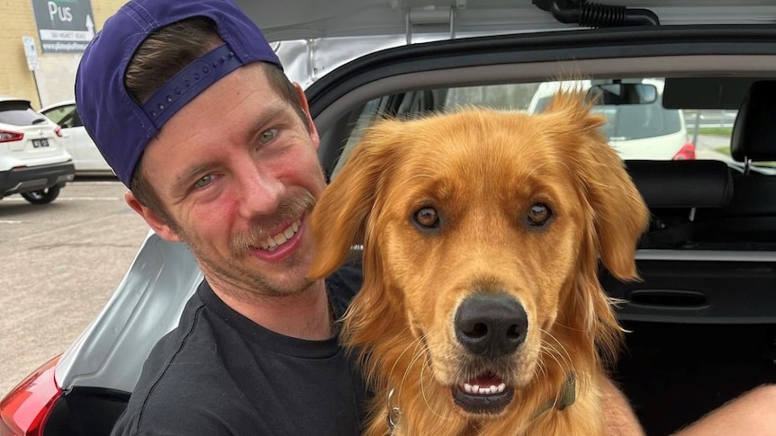 A man smiles while holding a golden retriever dog