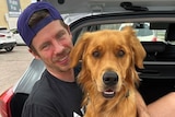 A man smiles while holding a golden retriever dog