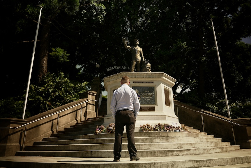 A man stands before a war statue.