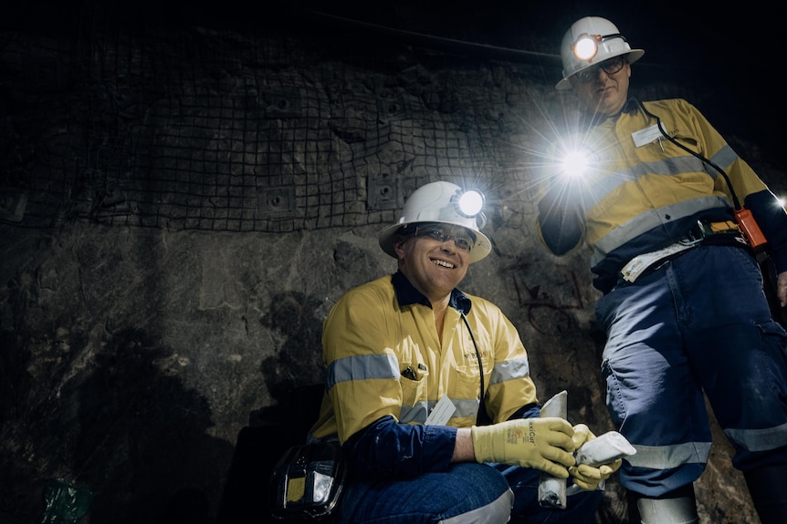 Two men in an underground gold mine wearing high-vis workwear and hard hards with lamps turned on.